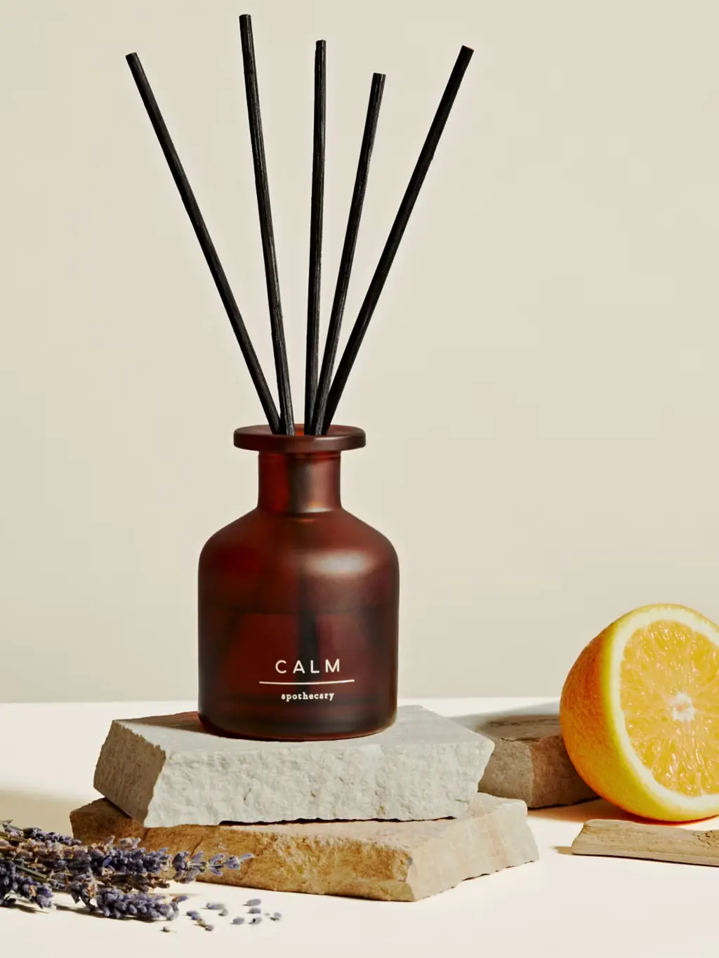 Calm diffuser sitting on a stone beside lavender and half an orange