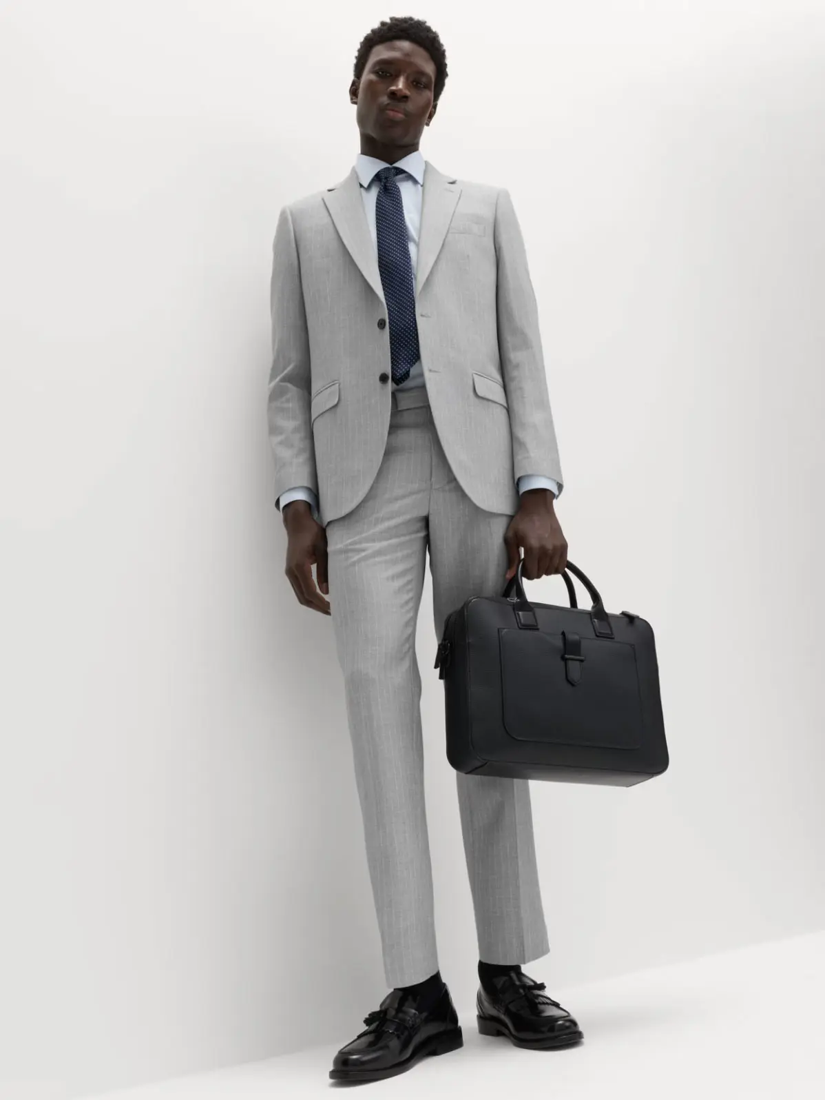Man wearing light grey suit with white shirt, blue tie and loafers