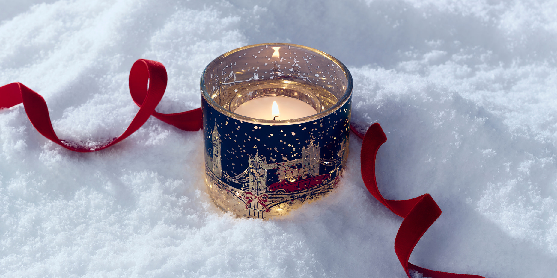 London-themed light-up candle in the snow beside a curled red ribbon