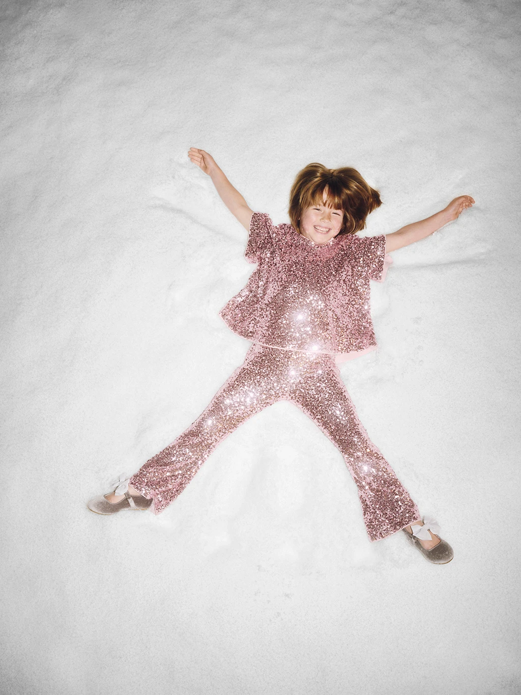 Girl wearing pink sequin party outfit making a snow angel