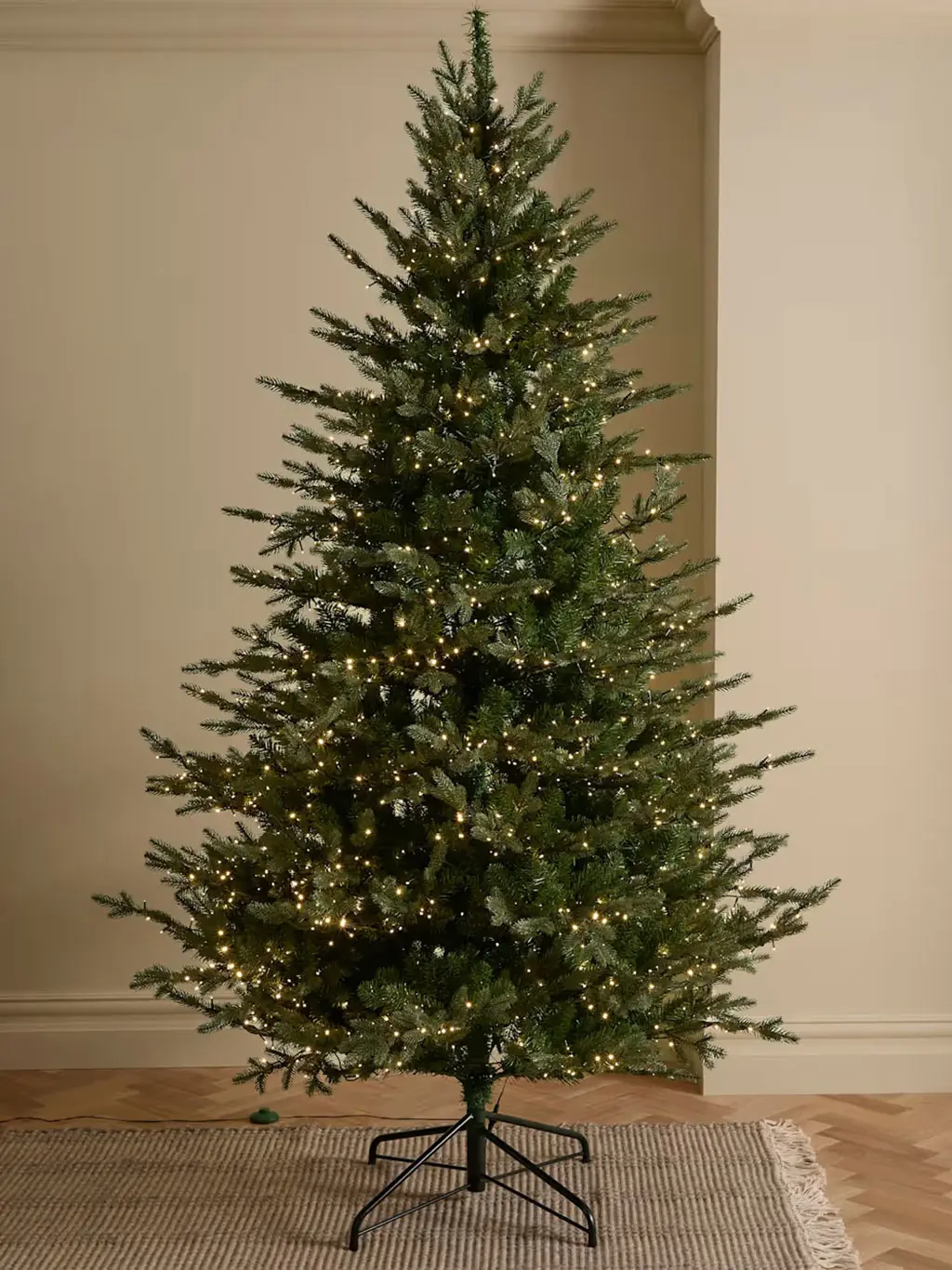 Large artificial fir Christmas tree with warm white lights and metal stand.