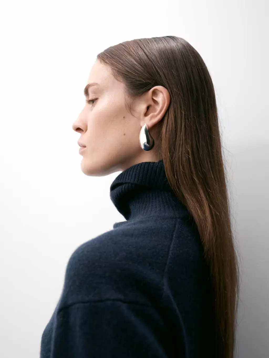 Woman wearing a navy roll-neck jumper with silver earrings.