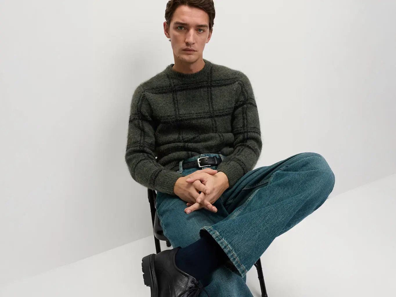 Man in a checked green jumper with blue jeans and a black belt