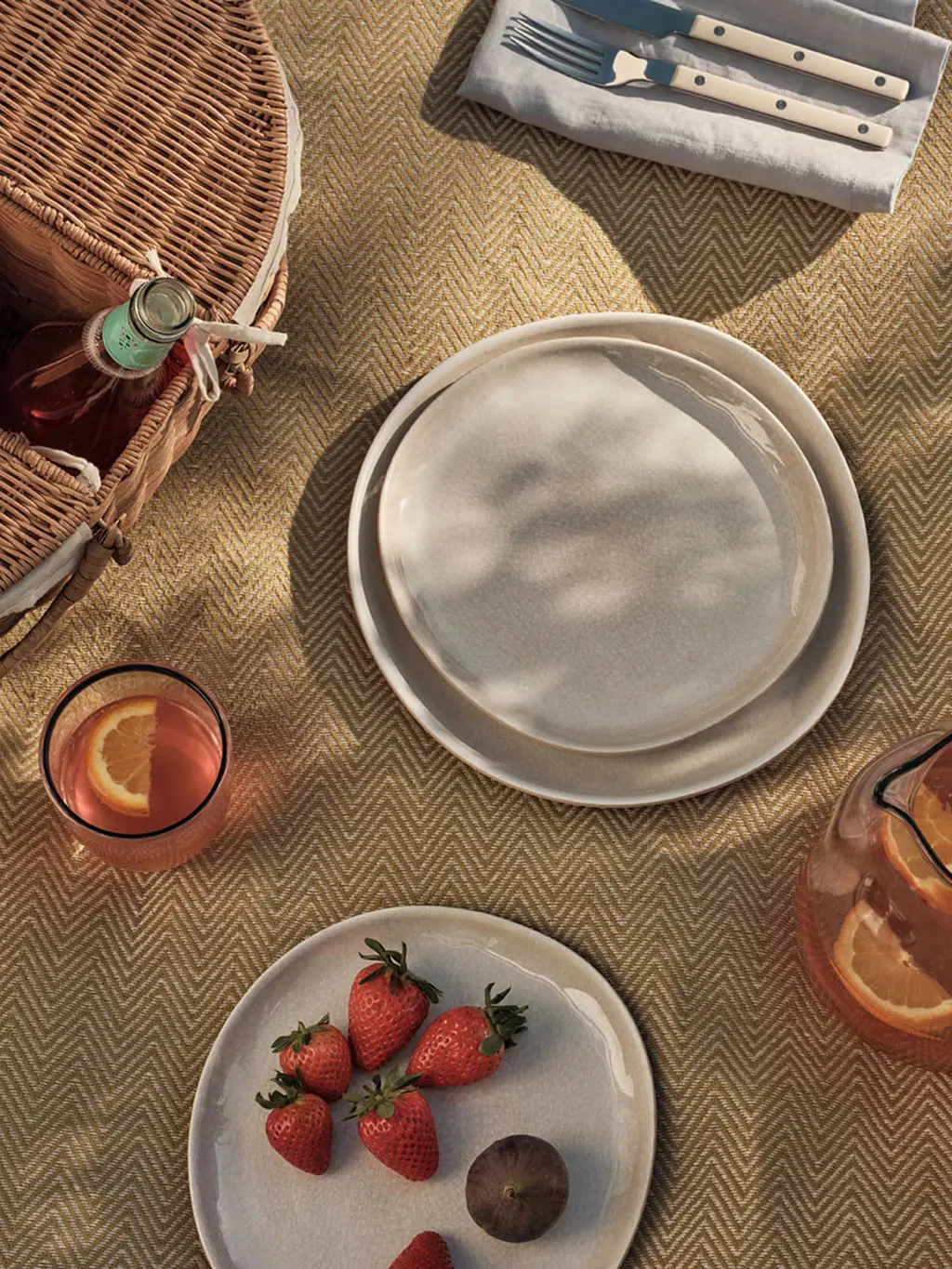 Picnic setup on a herringbone blanket with cream plates and a basket
