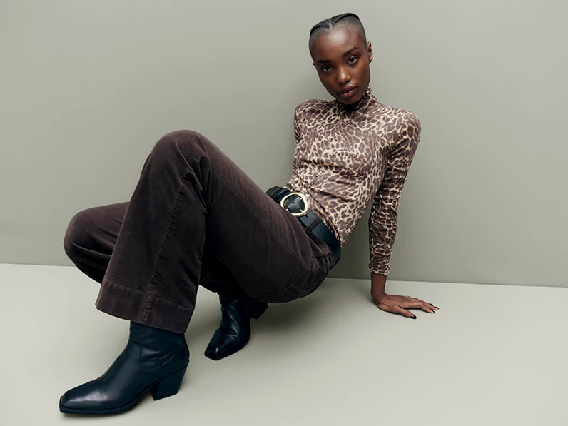 Woman wearing leopard print top, brown cords and black ankle boots