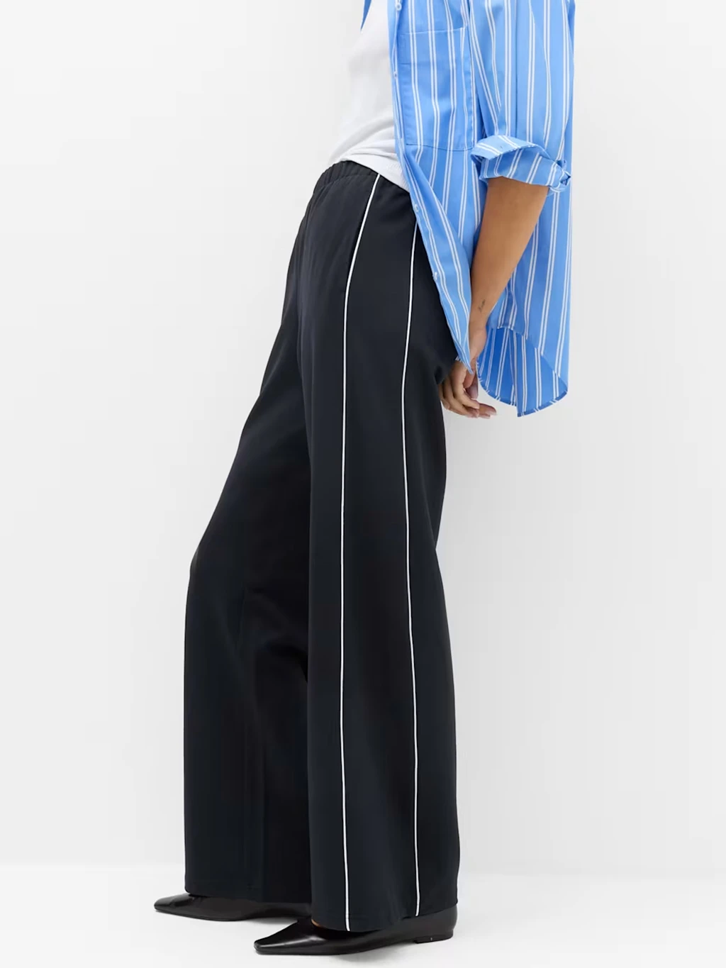 Woman wearing a pair of navy wide-leg joggers, white t-shirt and blue shirt.