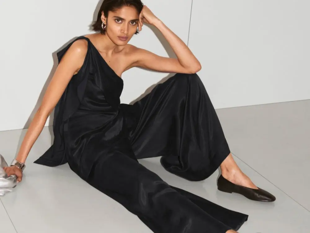 A woman sat on the floor wearing a black two piece outfit and ballet pumps