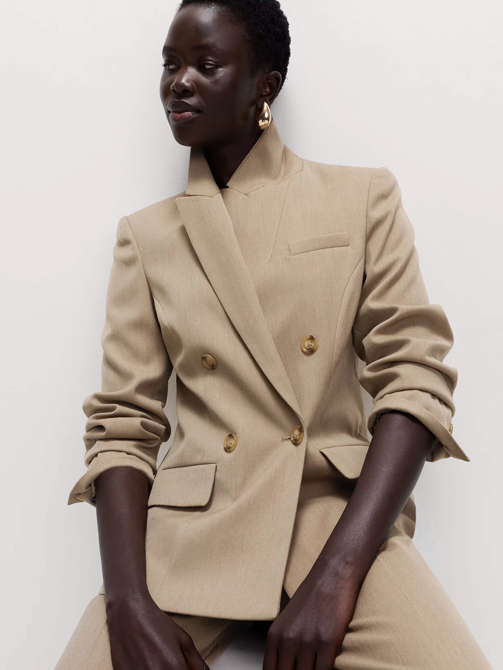 A woman wearing gold earrings with a beige trouser suit