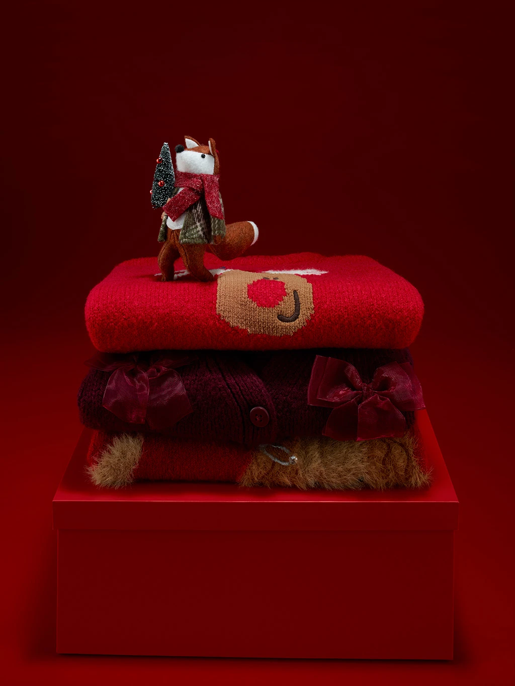 Group of kids' festive jumpers in a folded pile, with a felted mouse decoration on top.