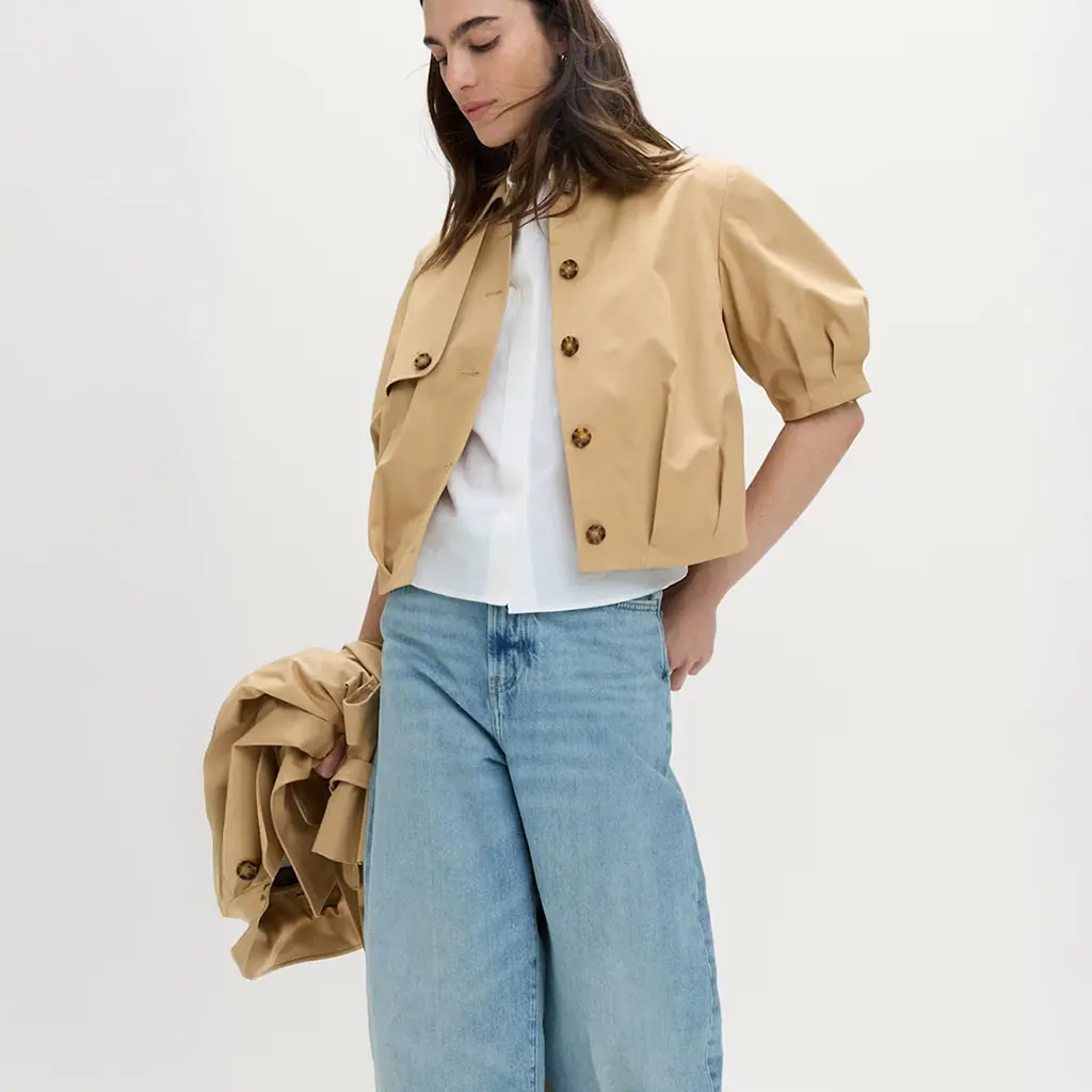 Woman wearing a white shirt, blue jeans and a camel jacket