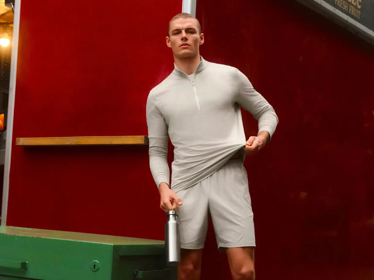 Man wearing neutral half-zip sports top and matching shorts, holding chrome water bottle 
