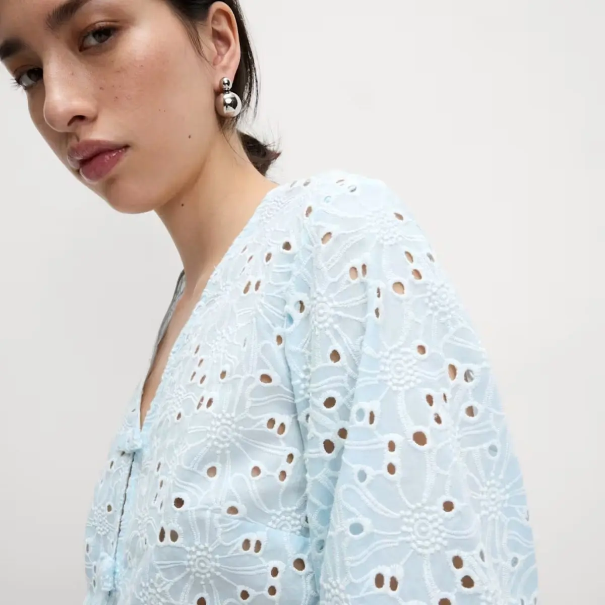 A close up of a woman wearing a baby blue floral cutout blouse