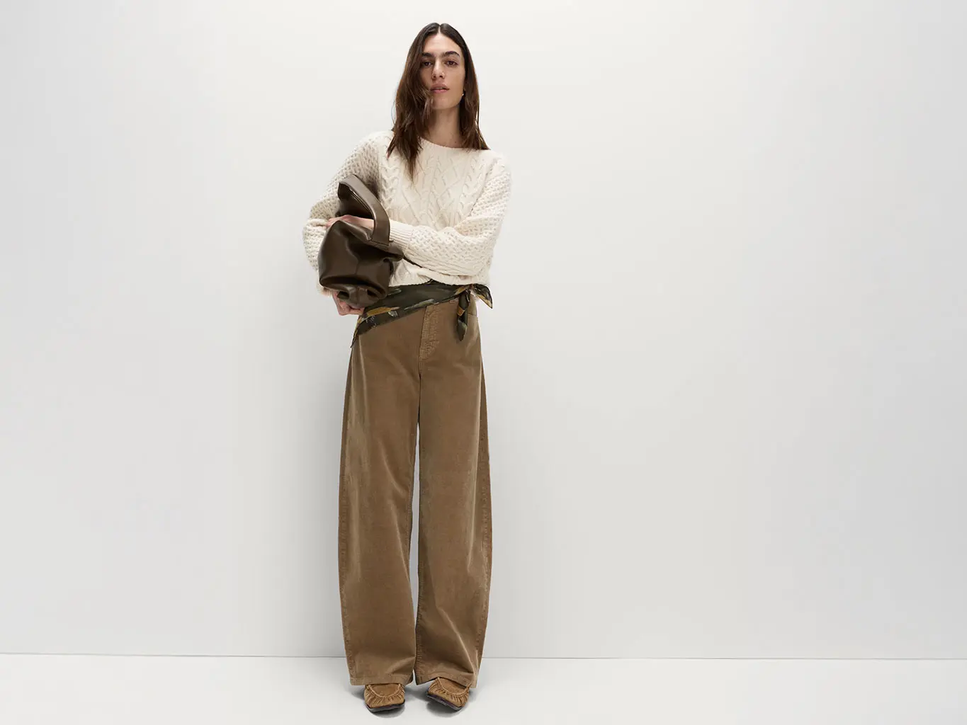 Woman wearing a cable-knit jumper with brown corduroy trousers, pumps and a brown tote bag