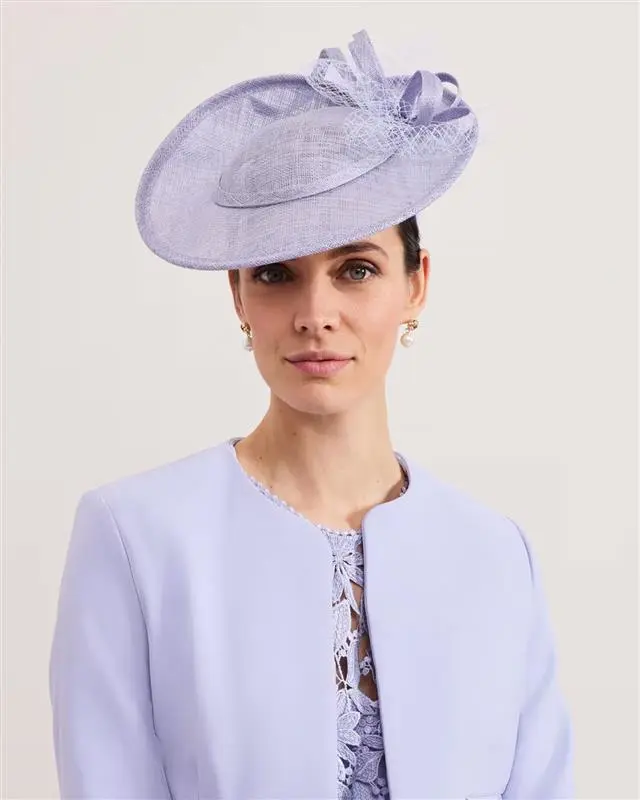 Woman wearing lilac fascinator, lilac collarless jacket and dress