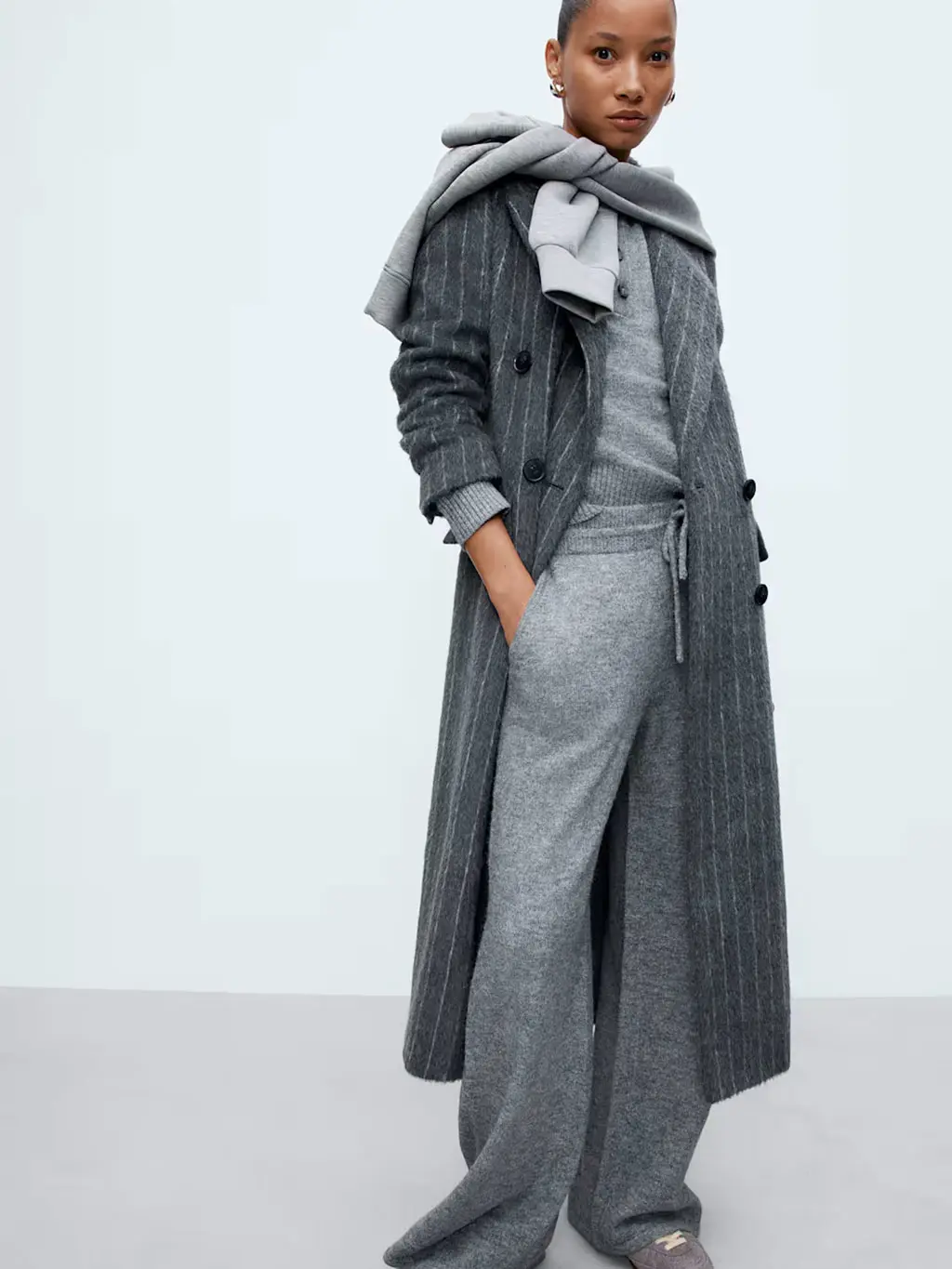 Woman wearing an all-grey loungewear set with a long striped coat and sweatshirt over the shoulders