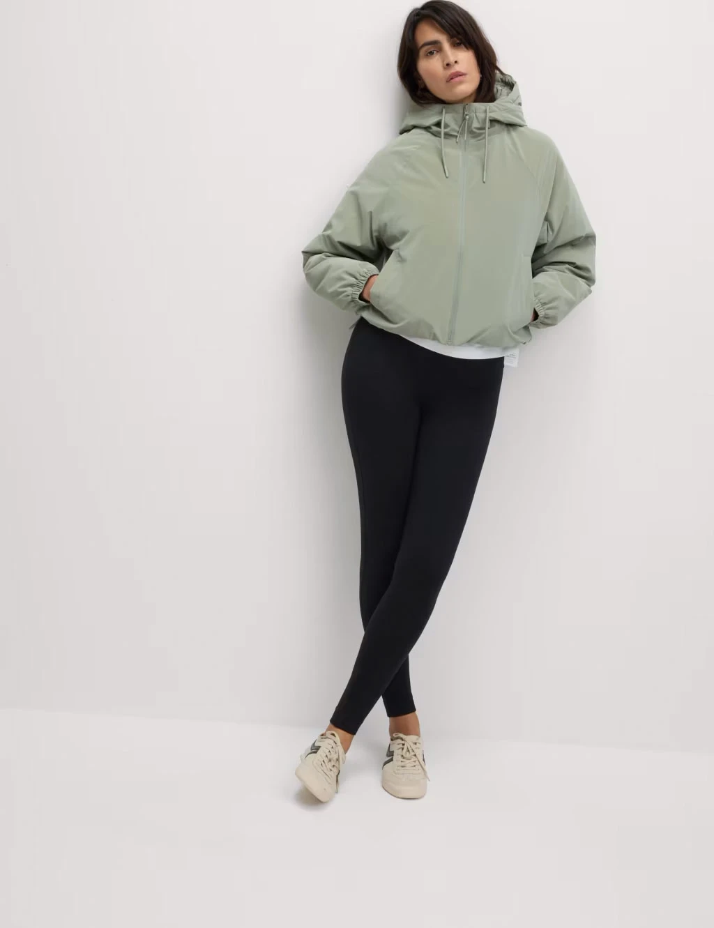 Woman wearing black leggings with a green zip-up jacket and white trainers.