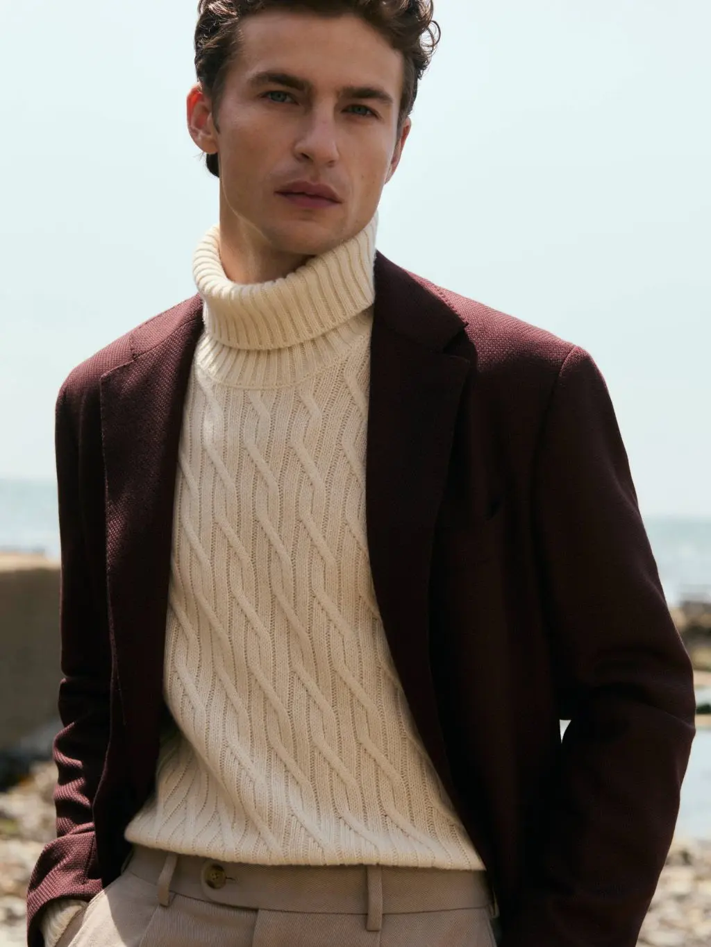 A man wearing a blazer and a cable knit jumper underneath