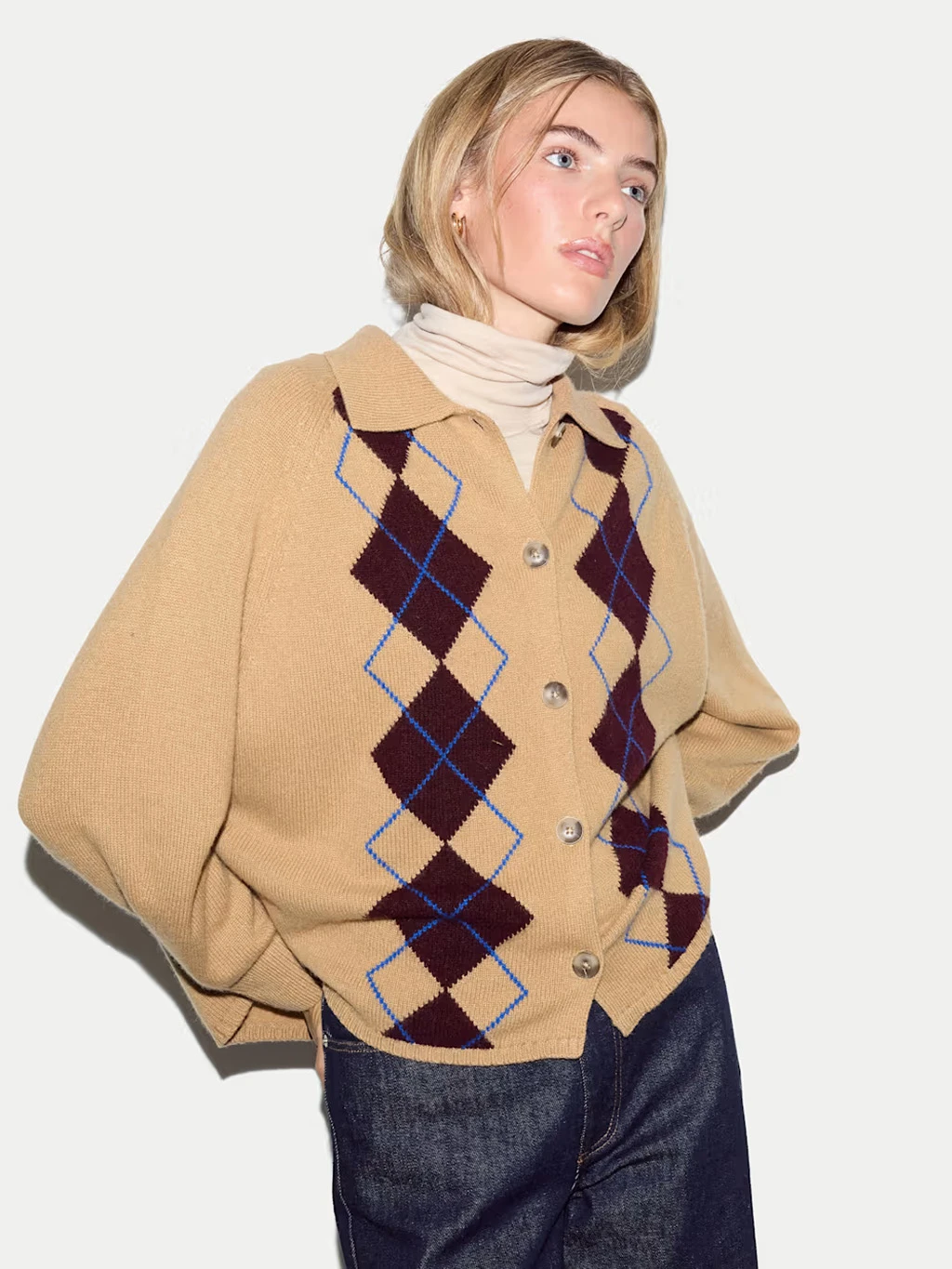 Woman wearing a beige argyle knitted cardigan and blue jeans.