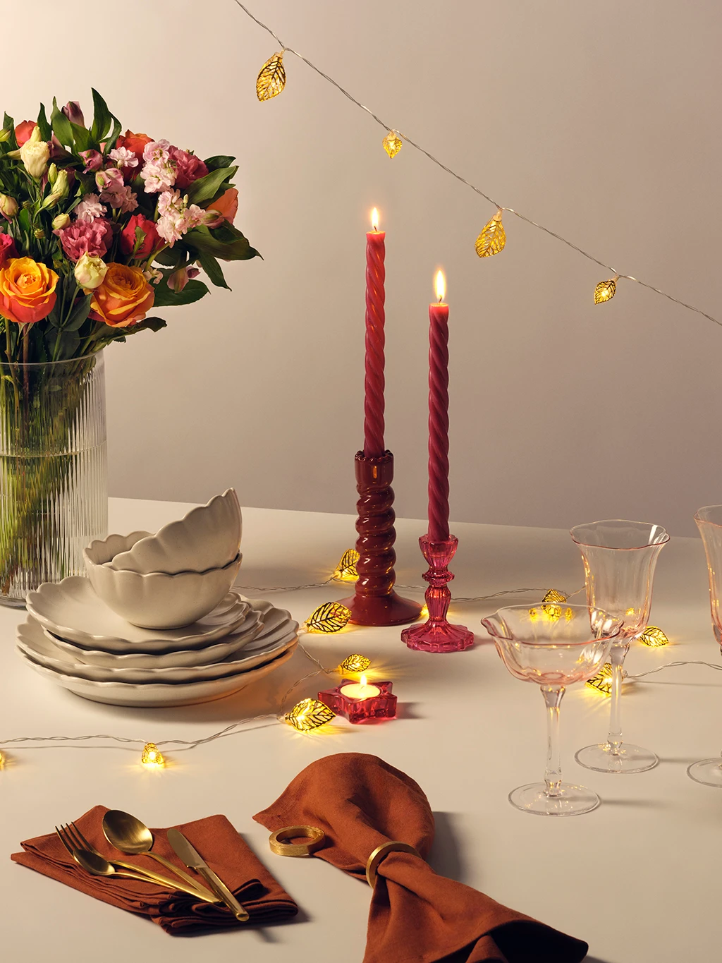 A table set with tableware, dinner candles, flowers and string lights