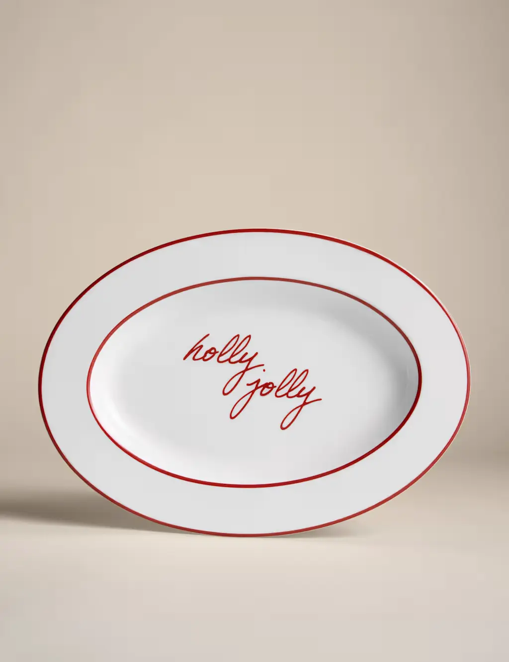 White ceramic serving platter with a red edge and red text that reads 'holly jolly'.