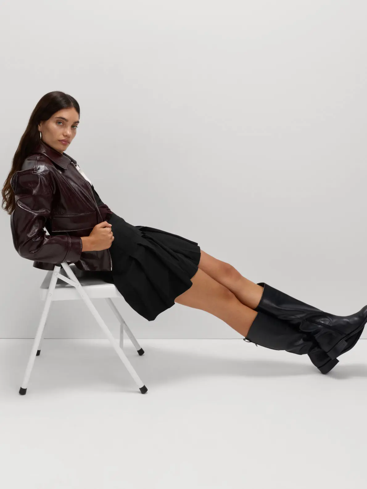 Woman sitting on a chair wearing brown leather jacket, black mini skirt and black riding boots
