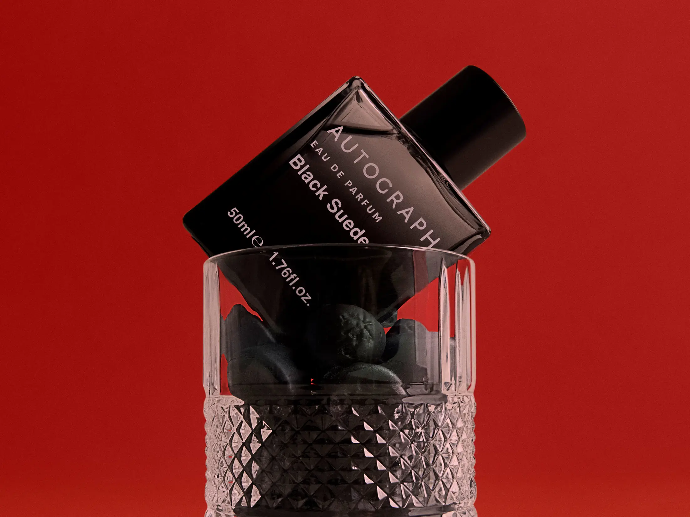 Glass holding men's Autograph fragrance in black bottle 