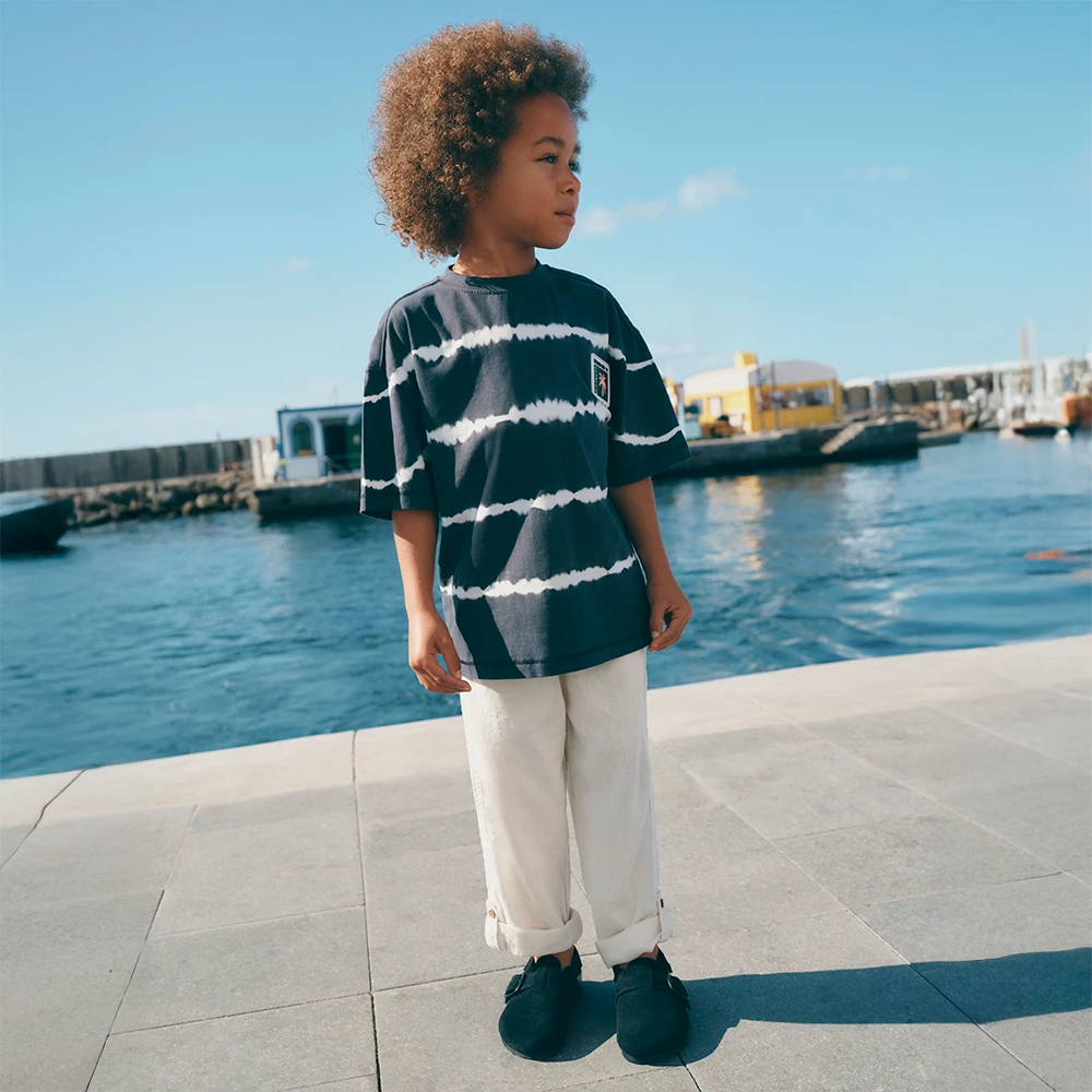 A boy wears a blue and white tie-dye T-shirt, white chinos and navy blue shoes