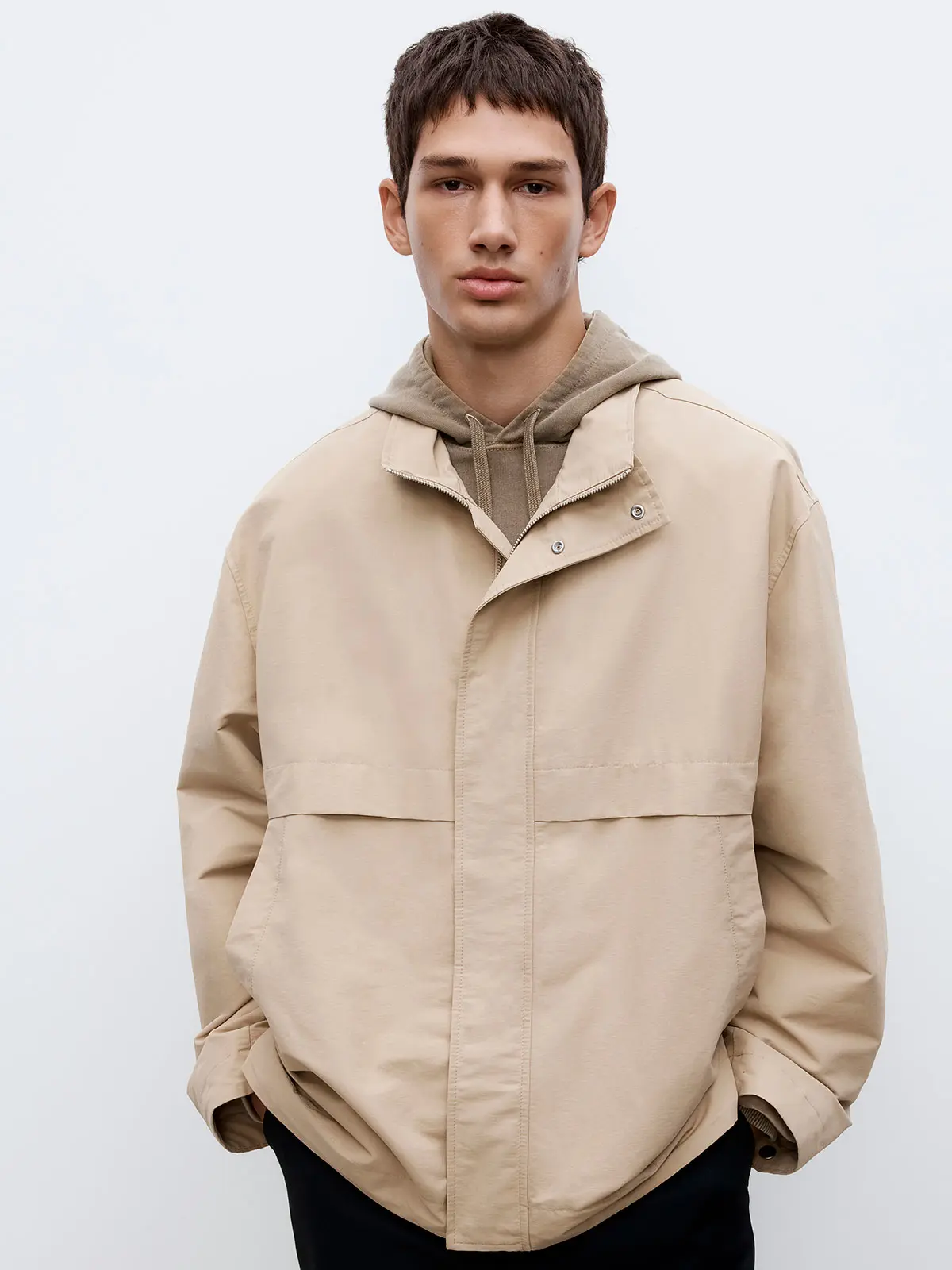 Man wearing cream windbreaker over green hoodie