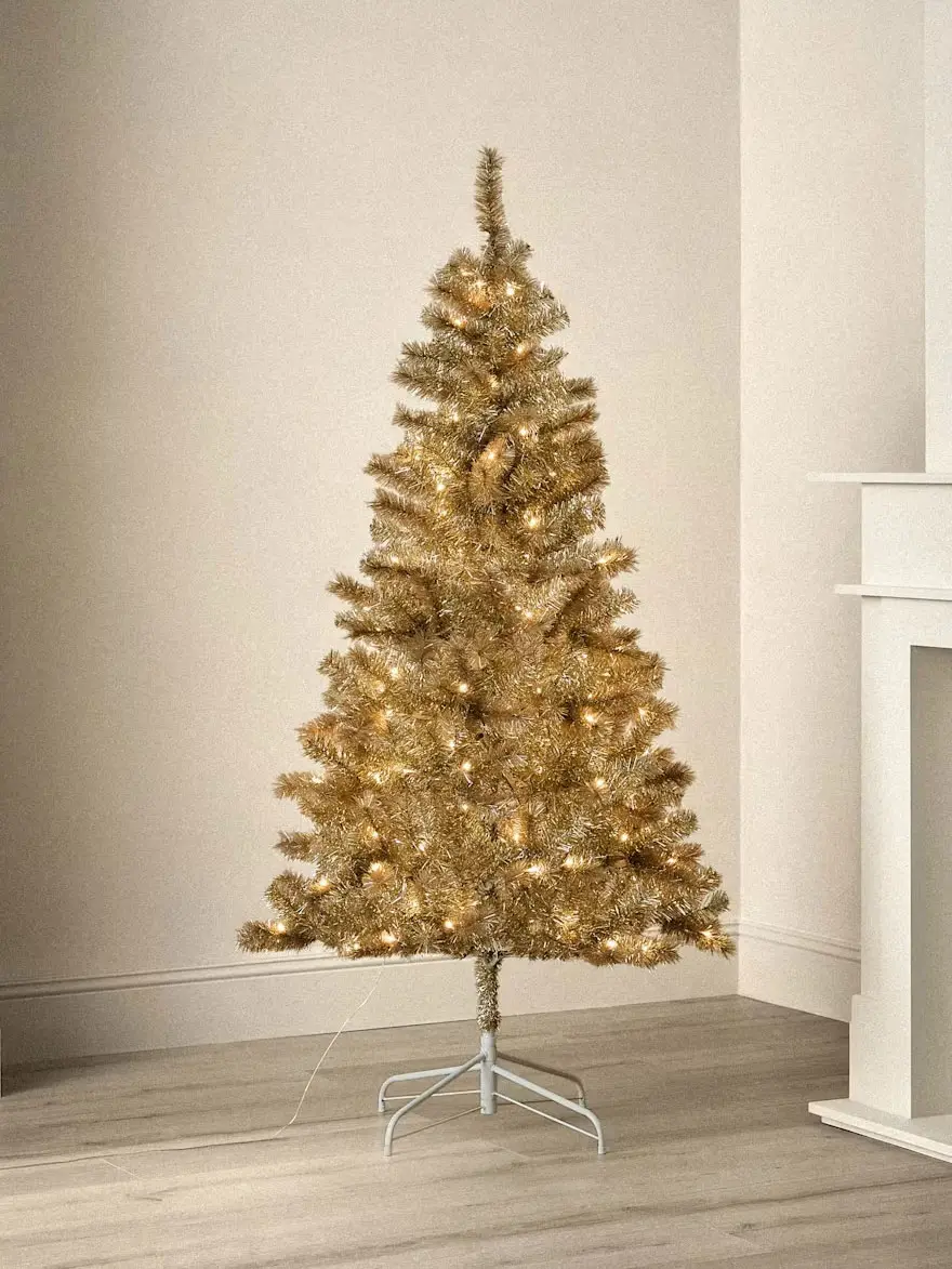 Gold artificial Christmas tree with warm white lights and metal stand.