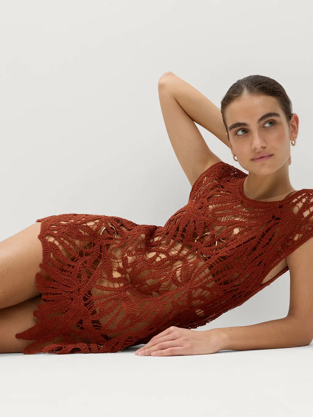A woman wearing an open-knit crochet dress over a black bikini