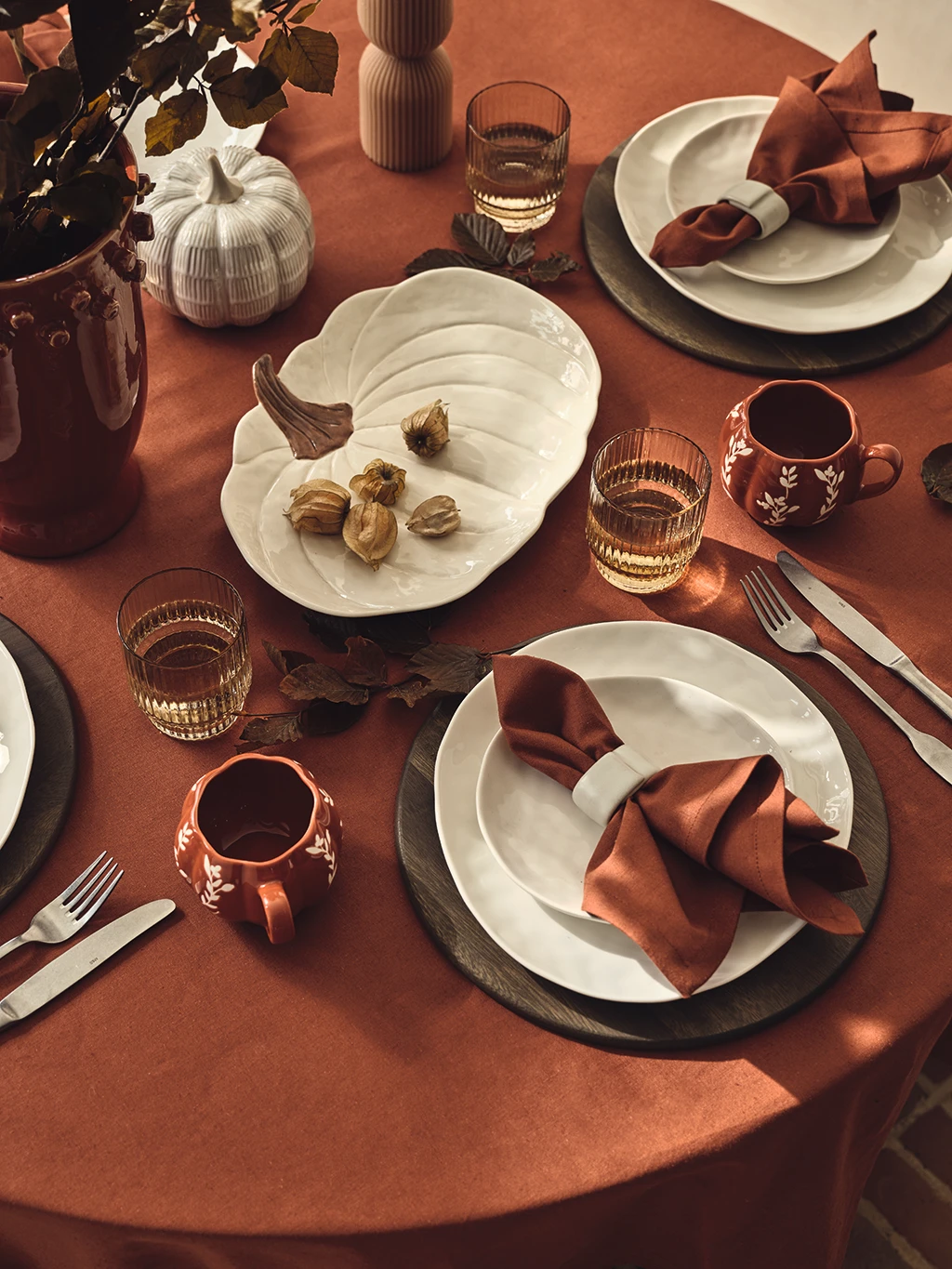 A table set with autumnal-coloured tableware, including a pumpkin platter