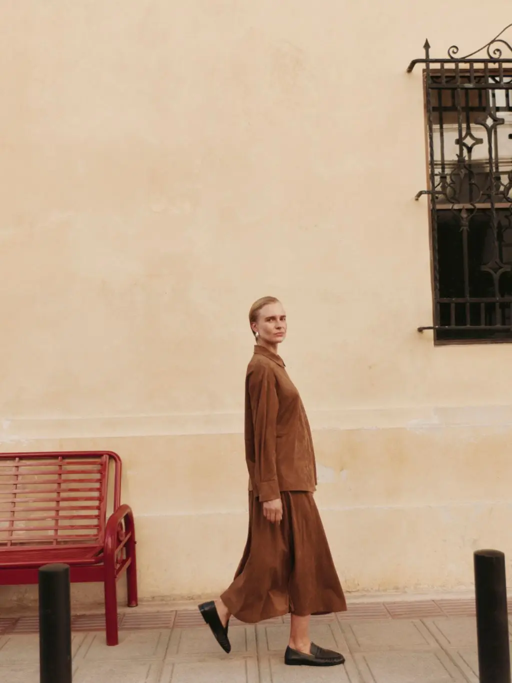 A model in matching shirt and skirt and loafers is walking on a pavement