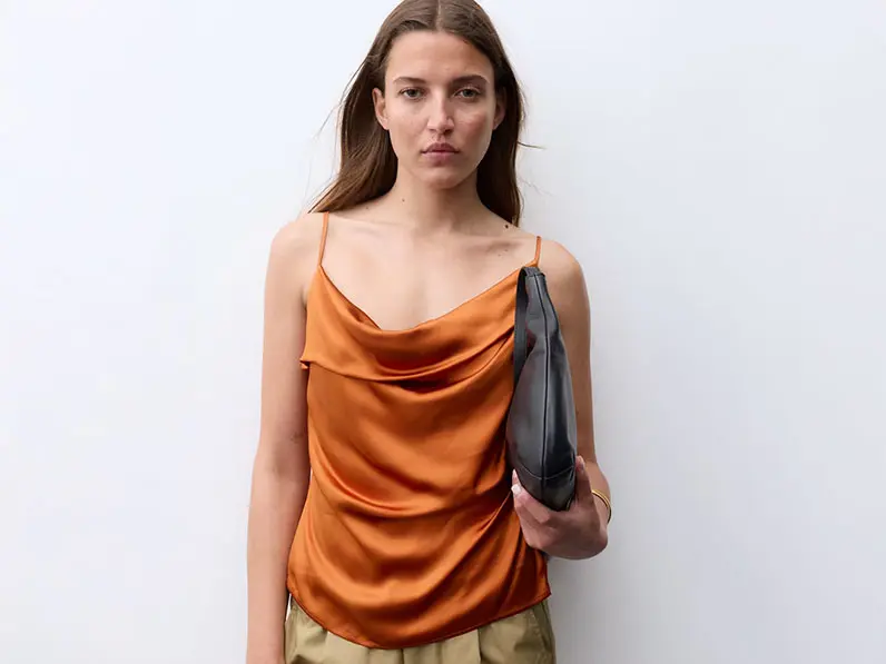 Woman wearing an orange cowl-neck top with green trousers