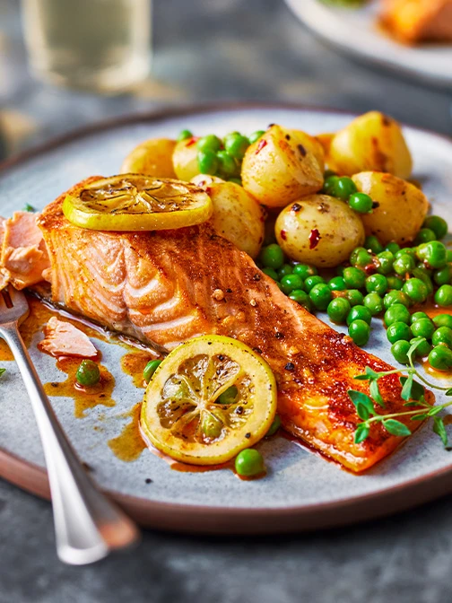 Salmon fillet with lemon slices, peas, chunky potatoes on grey plate with fork