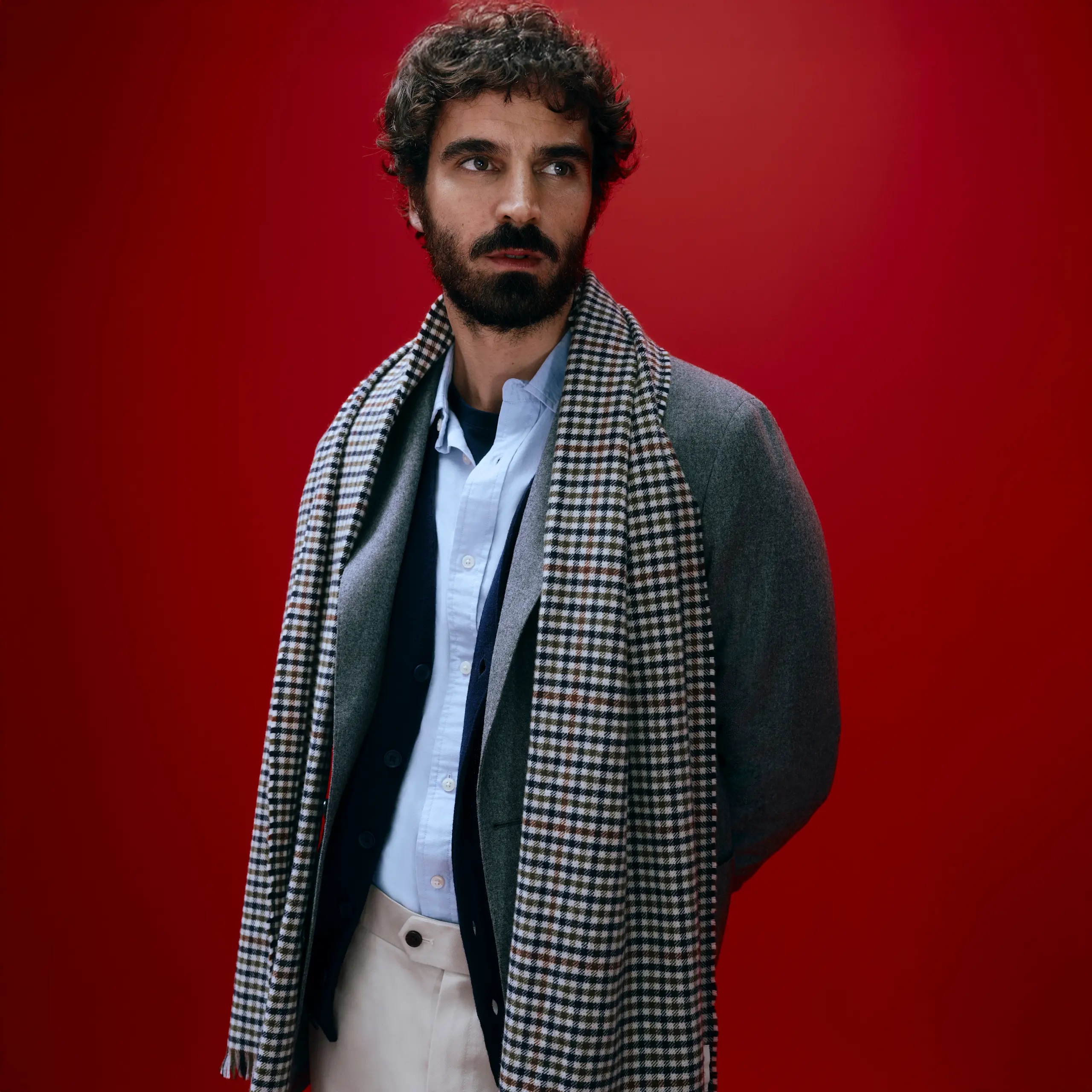 Man wearing a blue shirt, beige trousers, grey coat and a checked scarf