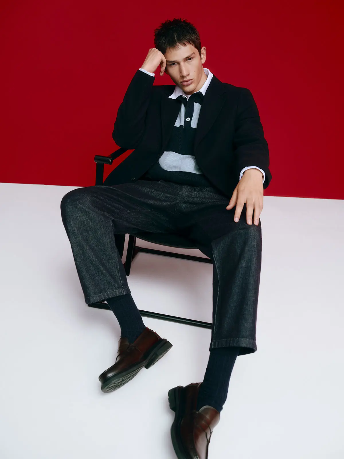 Man sitting on chair and wearing blazer over striped polo and jeans