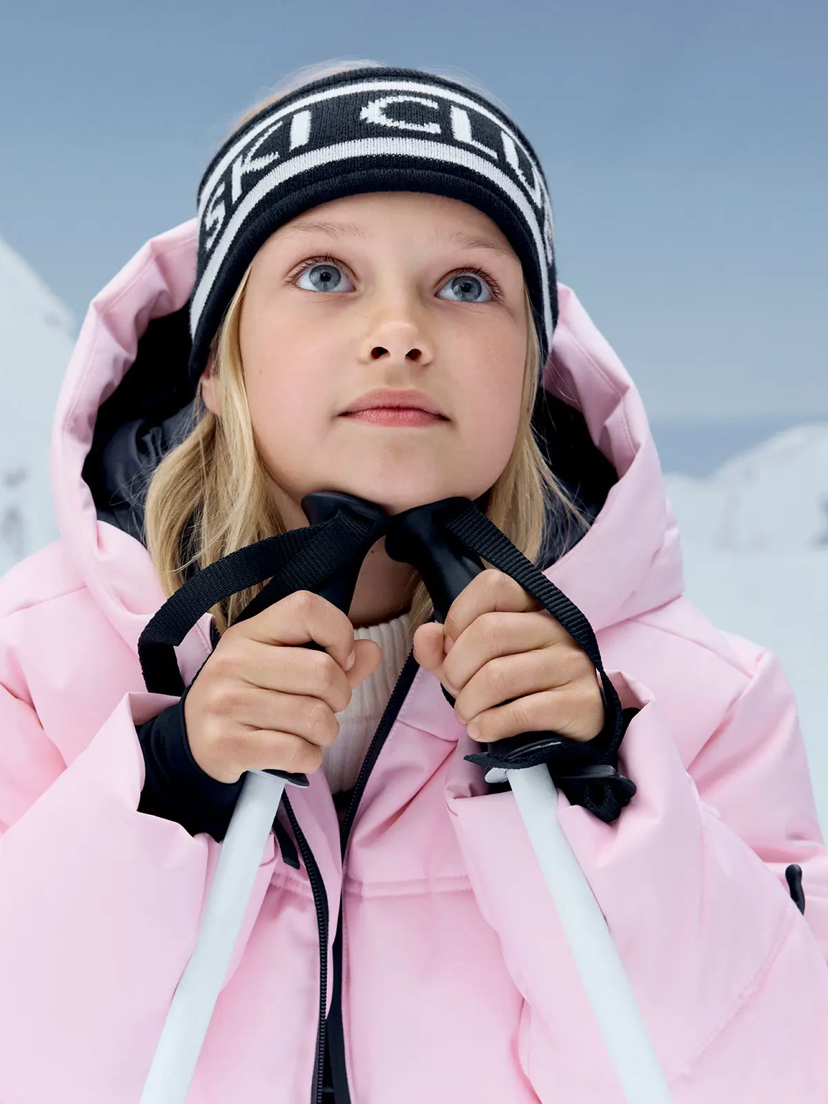 Girl wearing pink ski jacket and hat with slogan in white, holding ski poles
