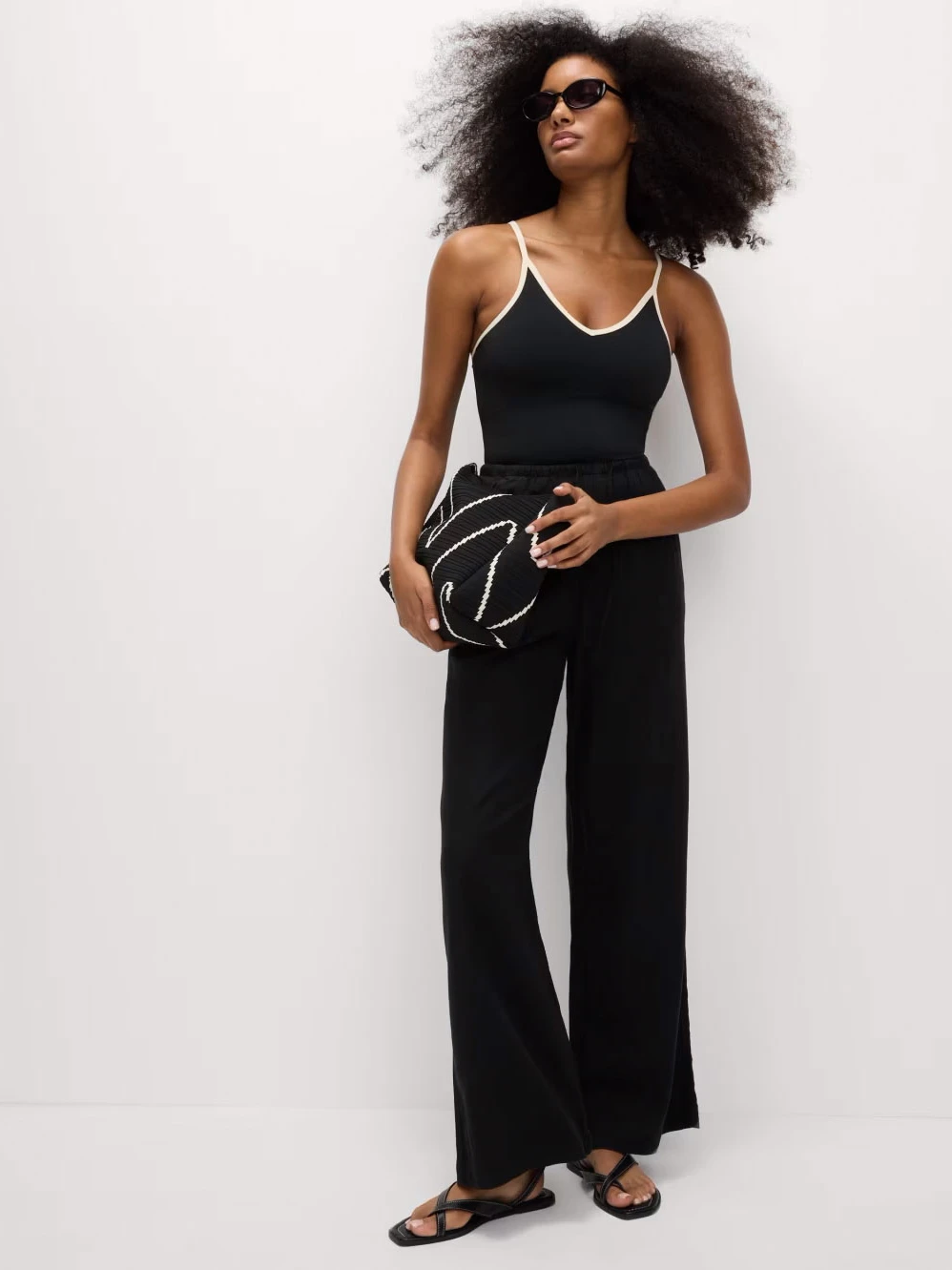 Woman wearing black trousers with a black vest top and sandals