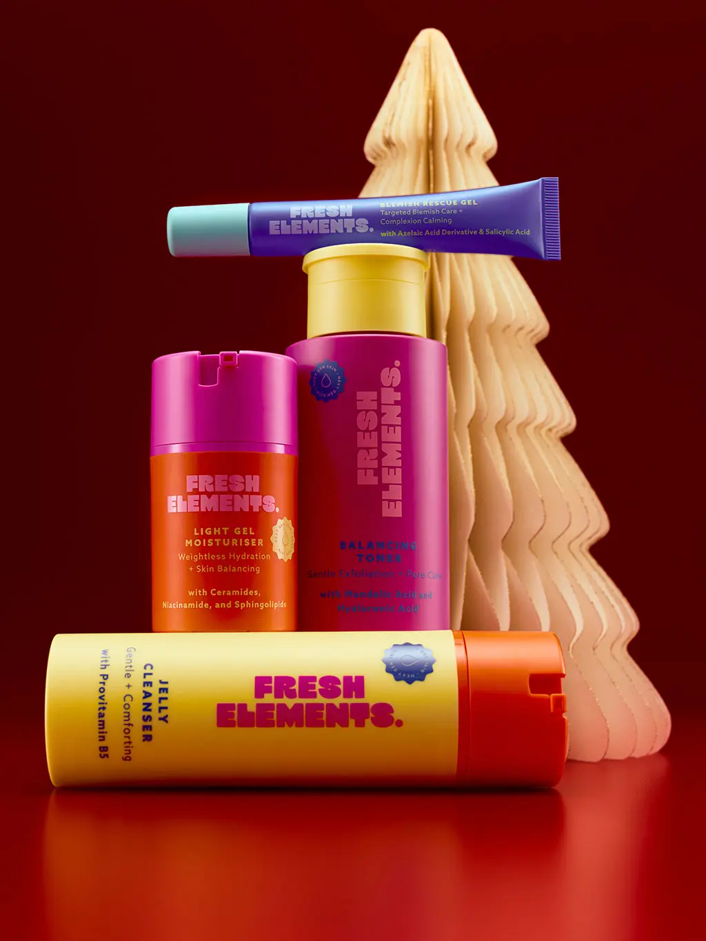 Group of Fresh Elements skincare products on a red background in front of a paper tree decoration.