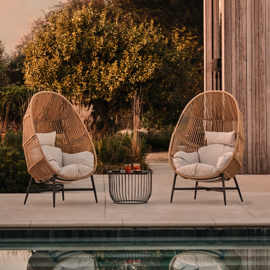 Two egg-shaped garden chairs with a black table between them. Shop garden chairs