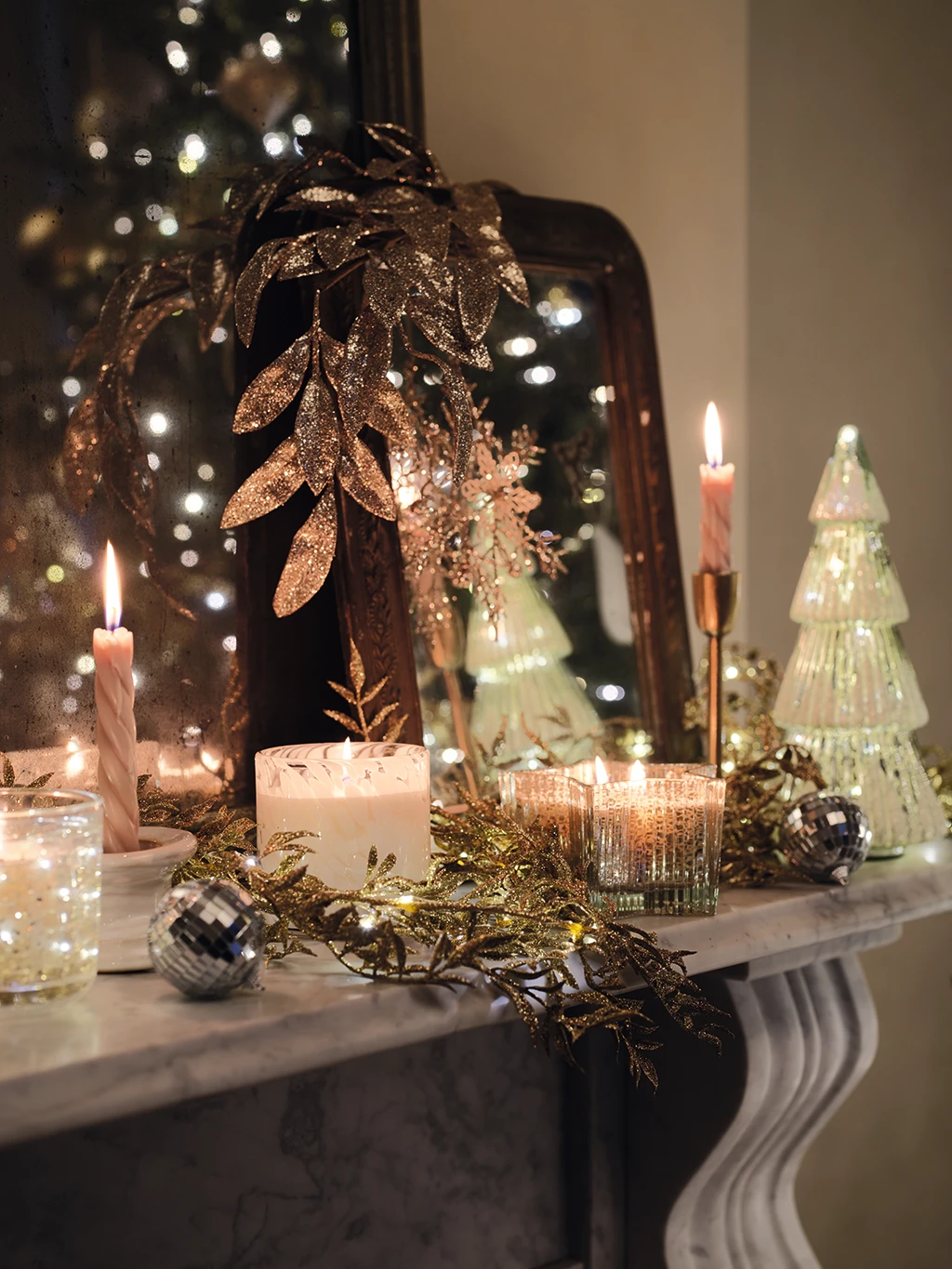 Assorted sparkling Christmas decorations and candles on a mantelpiece