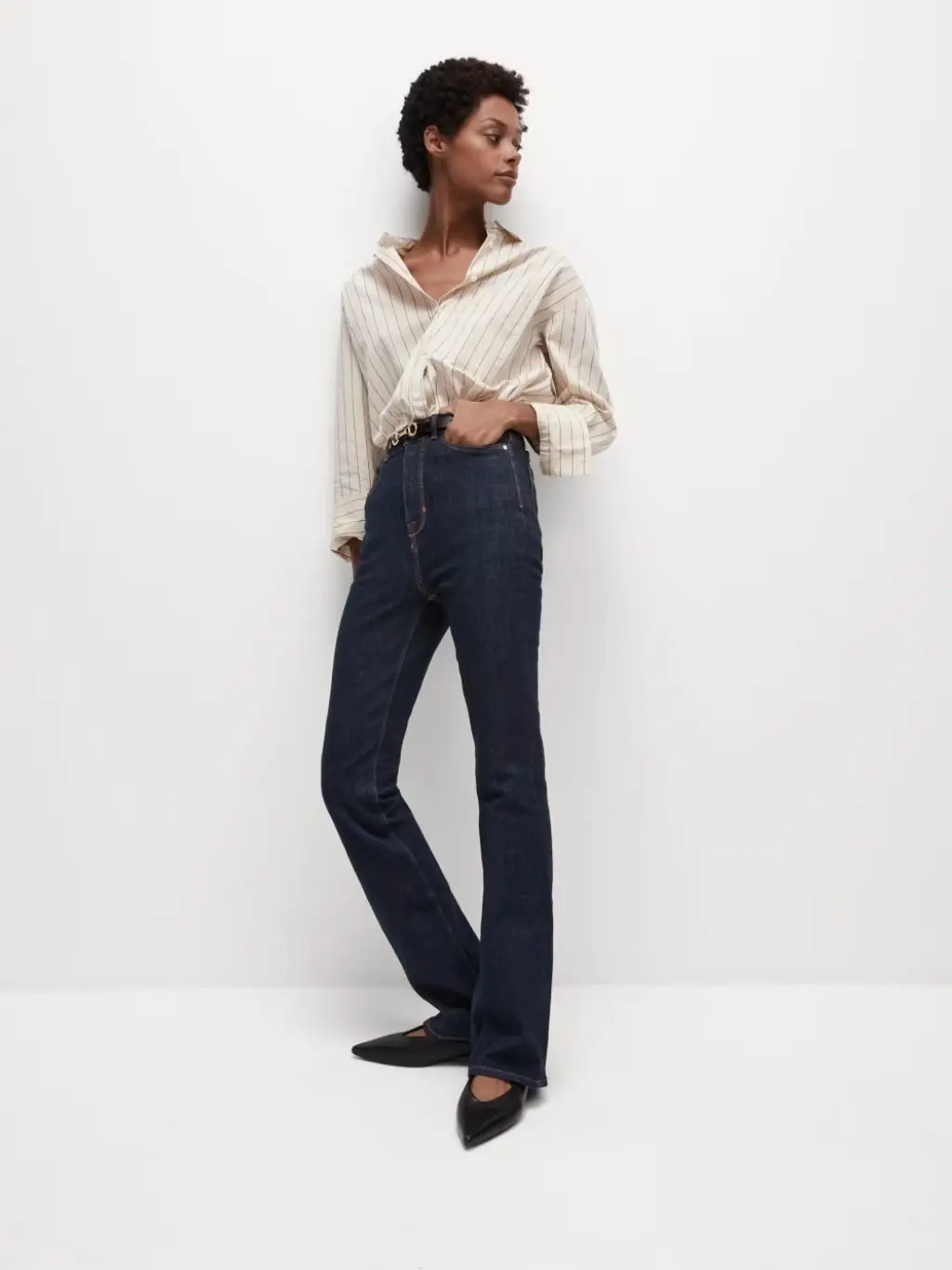 A woman wears dark indigo slim flared jeans and stripe shirt