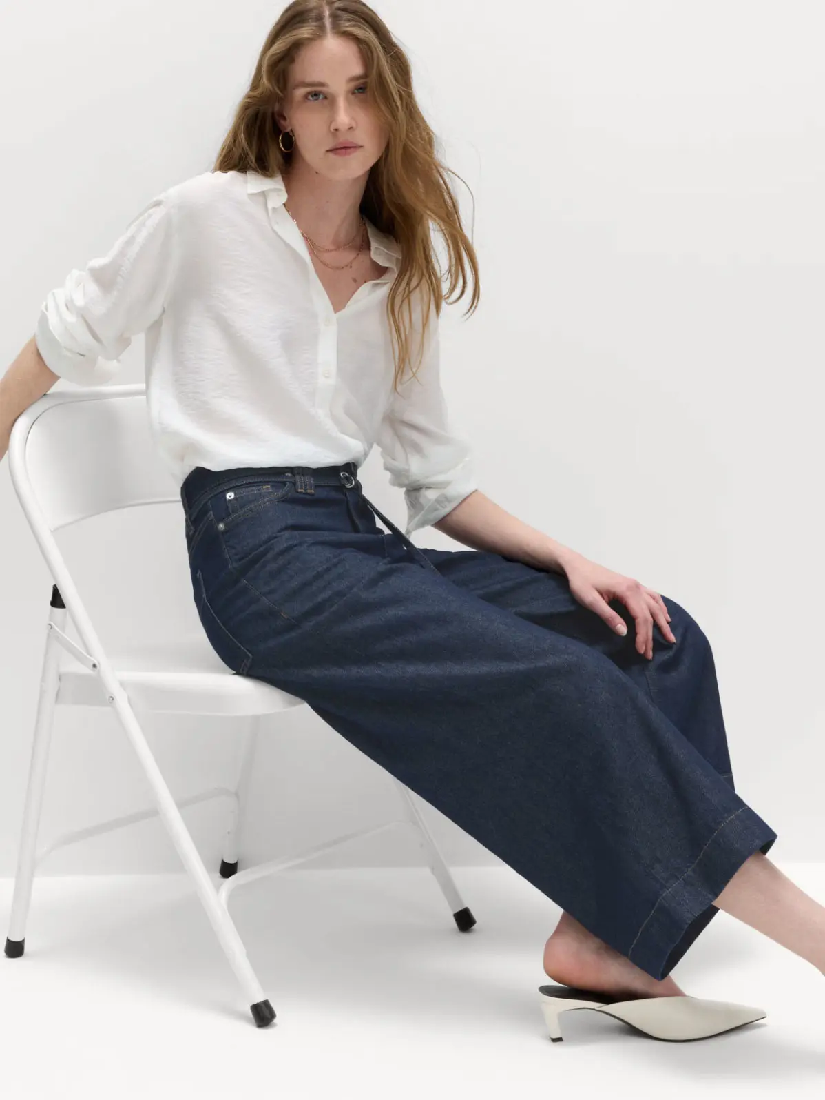 Woman wearing white top tucked into blue wide-leg jeans, paired with white pointed kitten heels 