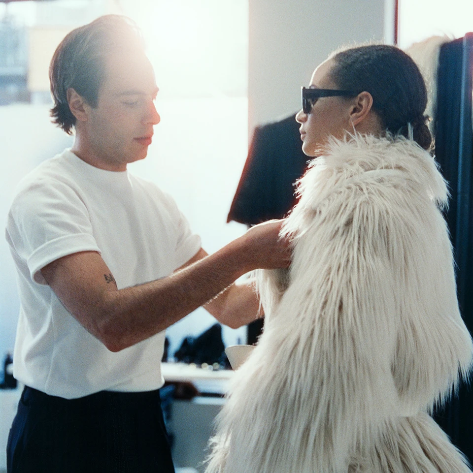 Marco Capaldi wearing a white T-shirt and black trousers; model wearing a white faux-fur coat and black sunglasses