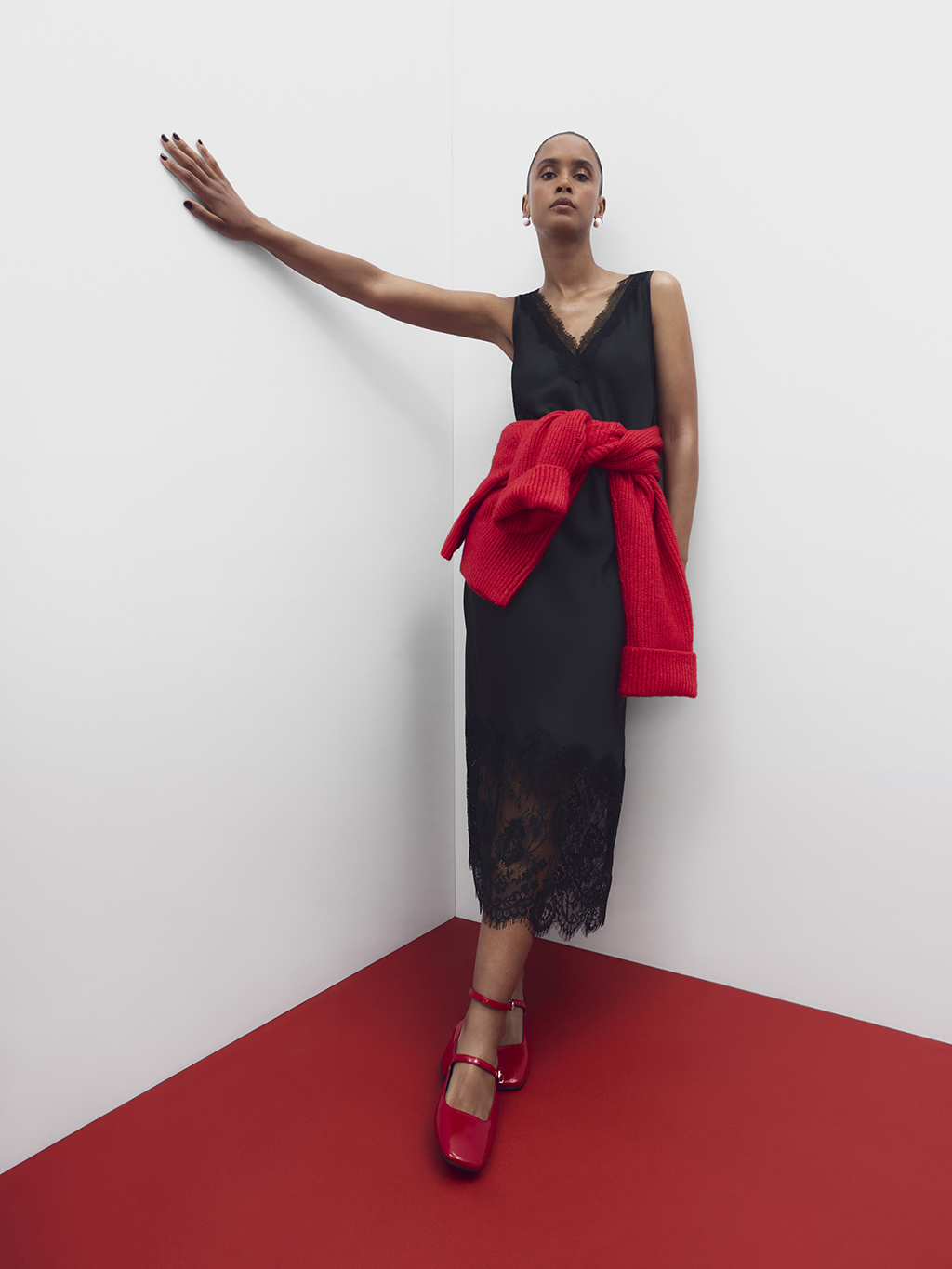 Woman wearing black lace dress with red jumper knotted at waist and red patent shoes