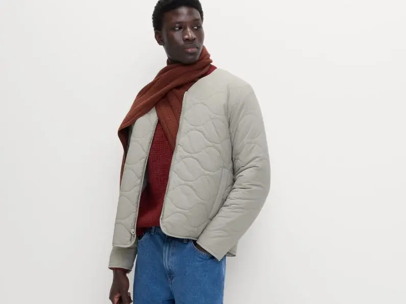 A man wears a quilted jacket with a scarf and jeans