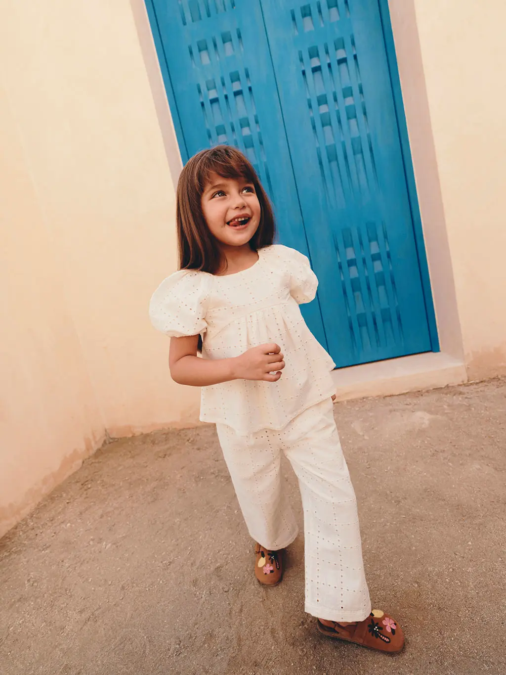 A girl wearing a white balloon-sleeve blouse with white jeans and sandals