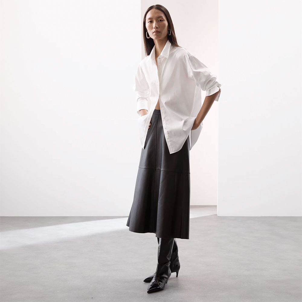 Woman wearing white cotton shirt, black leather midi skirt and black leather knee-high boots