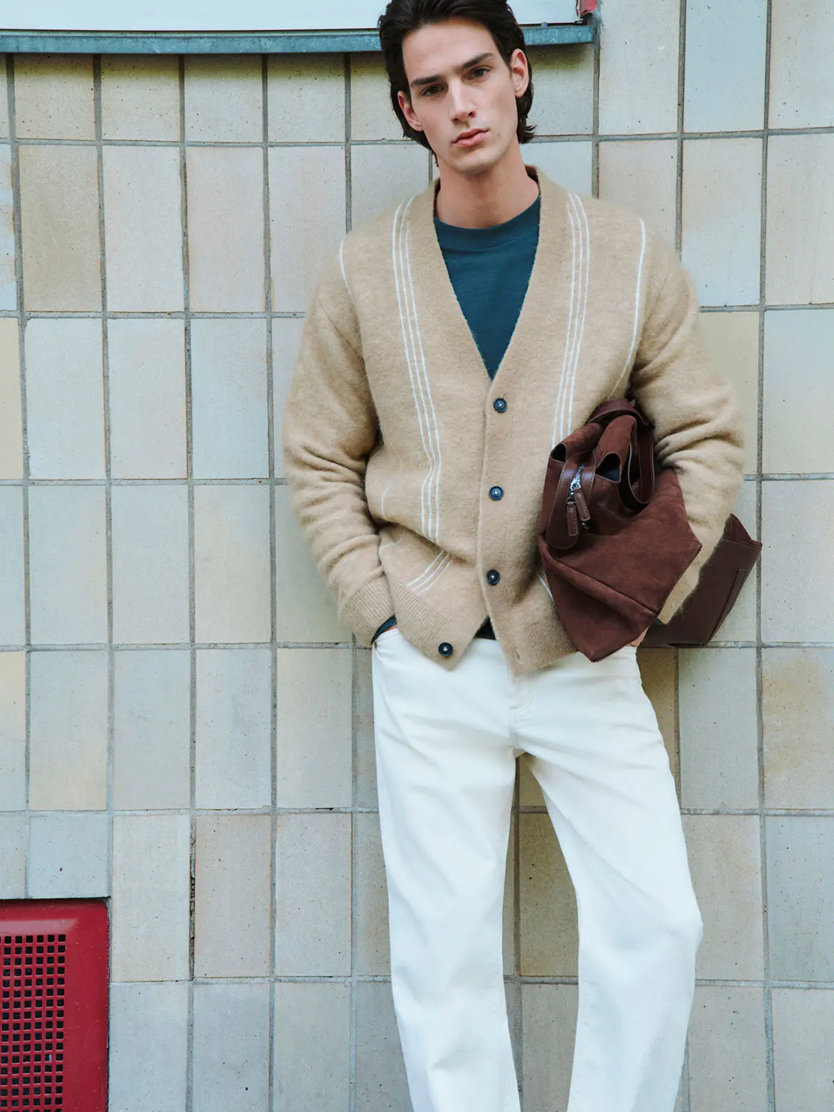 Man wearing neutral cardigan over blue T-shirt, paired with white jeans 