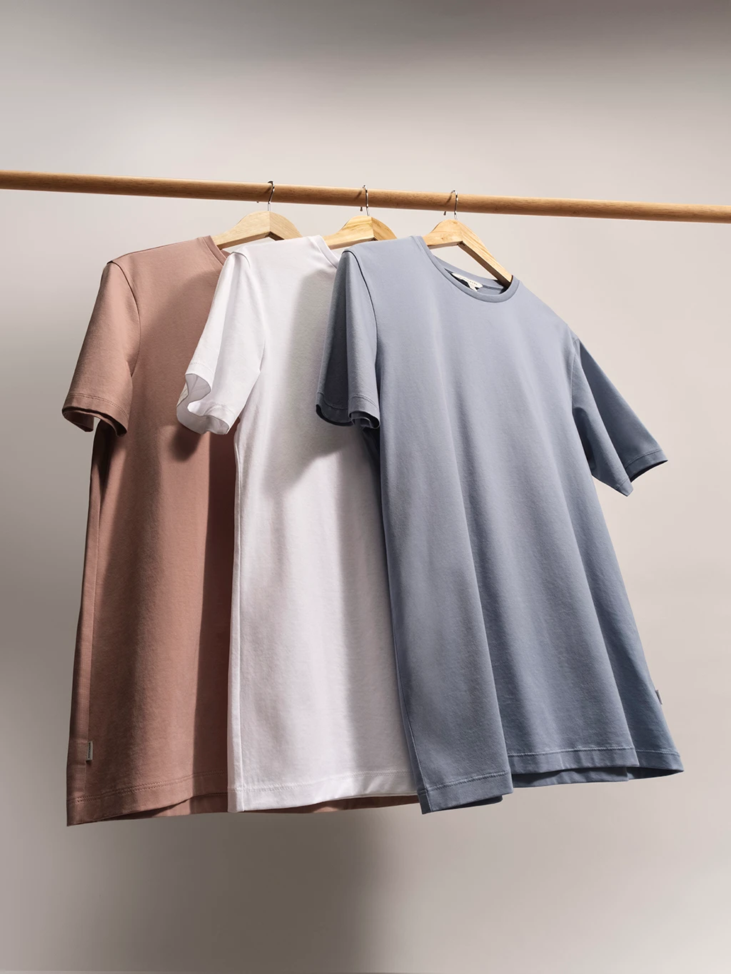 Three men's T-shirts in assorted colours hanging on a wooden clothes rail